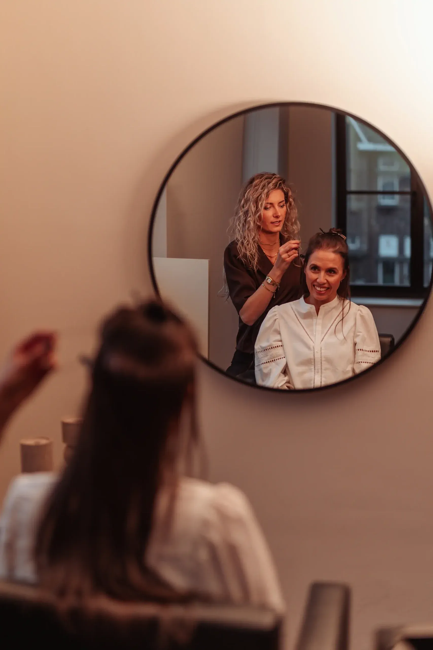Klant in de salonstoel, weerspiegeld in een ronde spiegel tijdens een consult bij Cèlia Blu